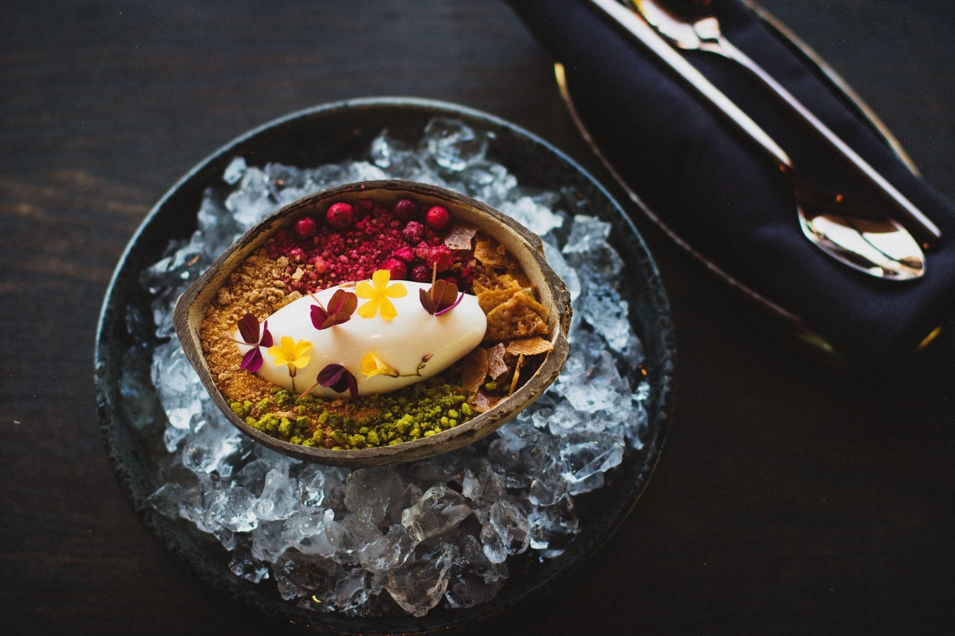 Uma sobremesa nórdica lindamente montada com sorvete, flores comestíveis e frutas silvestres, servida em uma tigela de gelo, representando o estilo culinário moderno de Copenhague.