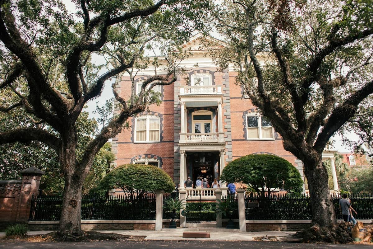 Large historic mansion with a romantic facade, framed by grand live oak trees and lush greenery, capturing New Orleans' garden district charm.