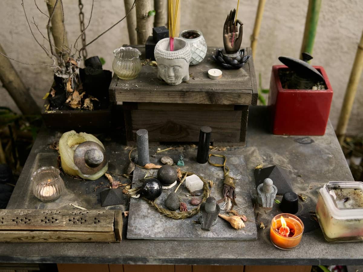 Altar o santuario al aire libre cubierto de velas, figuritas, piedras, objetos tallados e incienso, evocando prácticas religiosas populares.