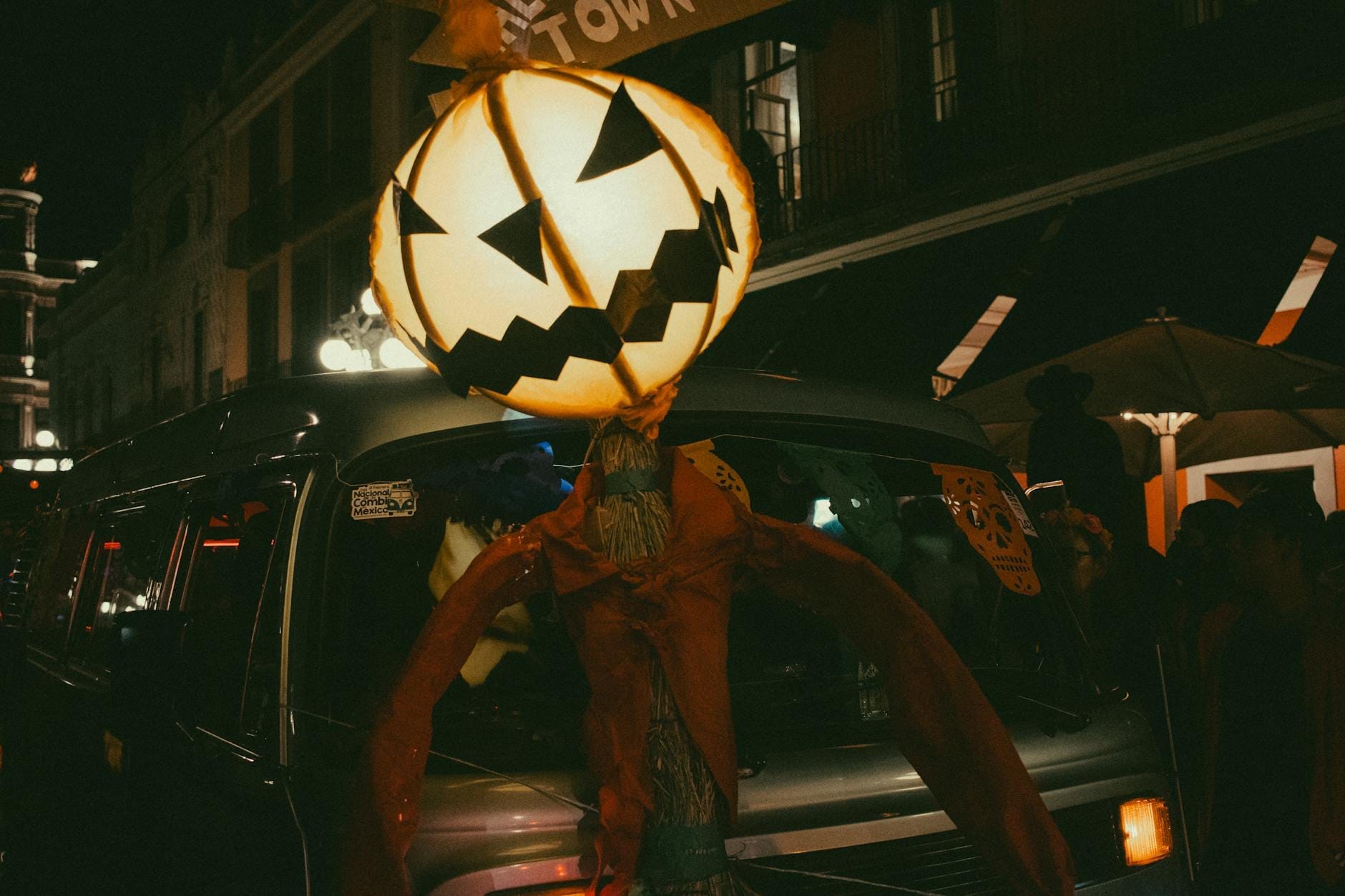 Grande abóbora luminosa com um sorriso largo contra um animado cenário noturno de rua, capturando o clima festivo do Halloween em Nova Orleans.