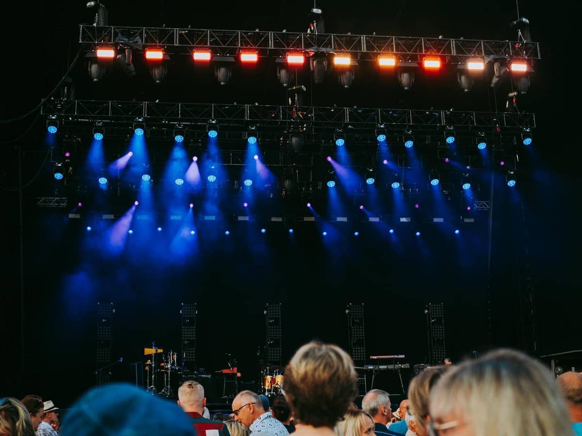 Outdoor music festival stage with colorful lights and an audience gathering in front, ready for a live performance.