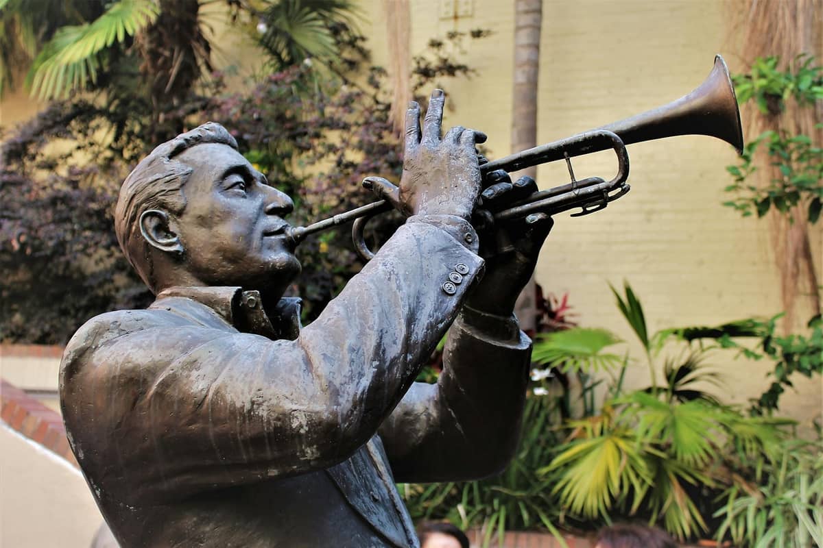 Close-up of a bronze statue of a trumpet player in a lush outdoor setting, evoking jazz heritage.