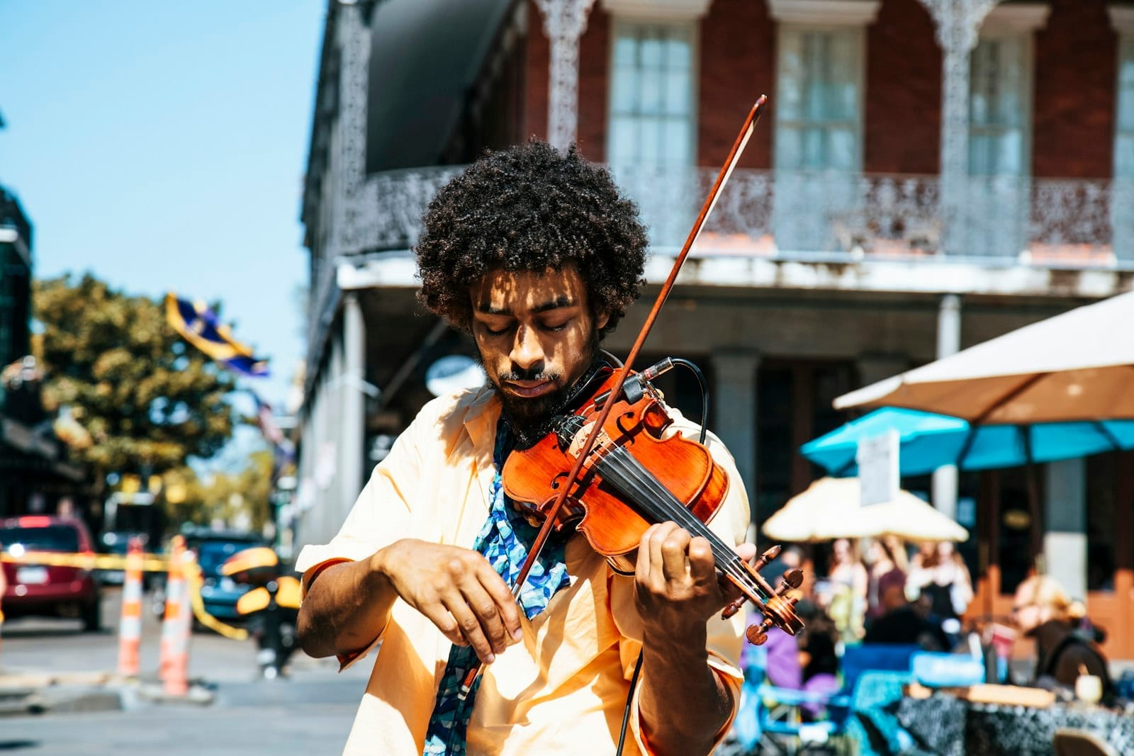 Músico de rua tocando violino no French Quarter de Nova Orleans, com varandas de ferro e guarda-chuvas coloridos em um dia ensolarado.