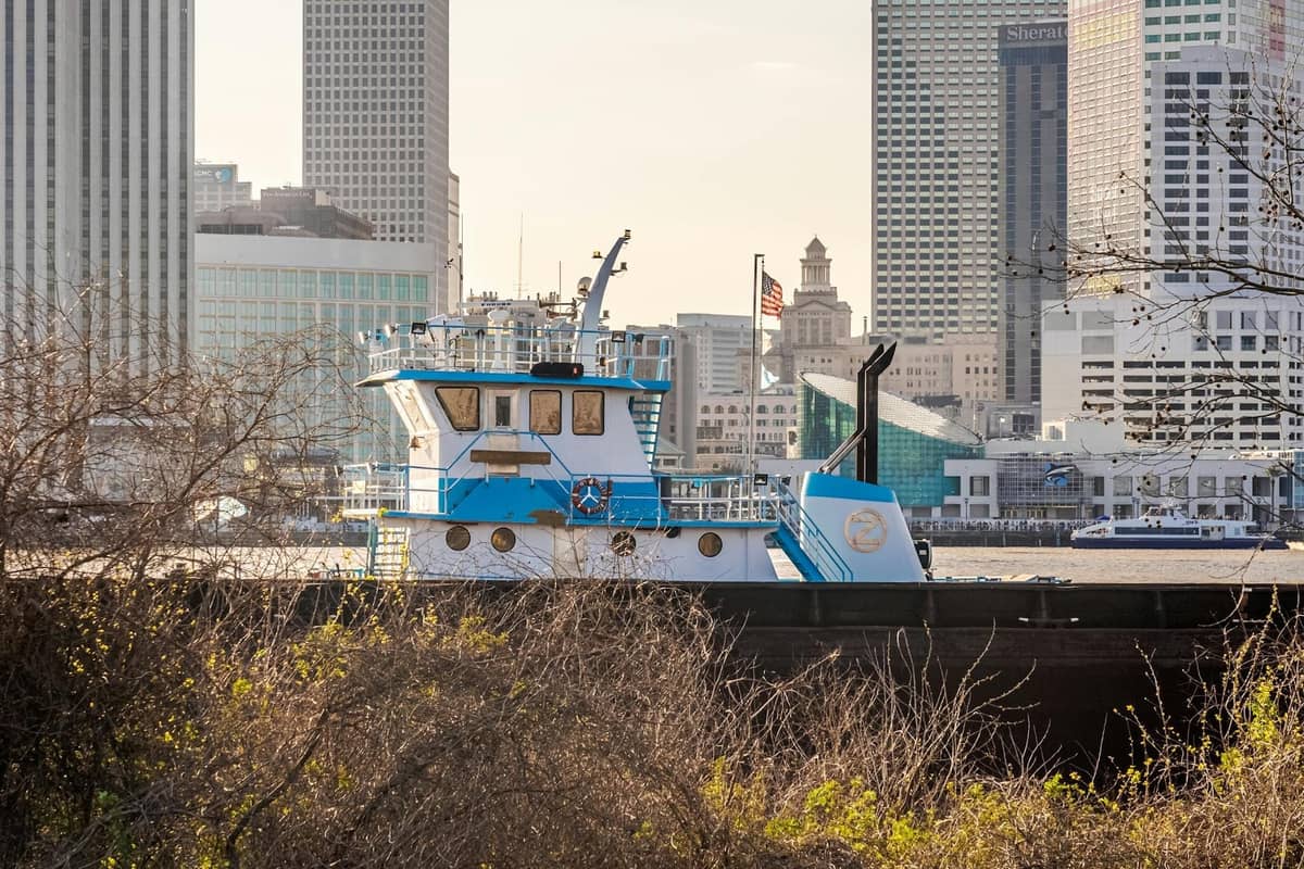 A tugboat travels along the river with downtown New Orleans skyscrapers in the background, symbolizing activity by the waterfront.