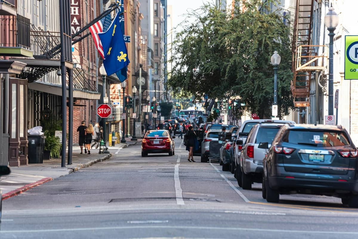 A busy downtown New Orleans street with parked cars, pedestrians, and flags, showing a lively urban environment.