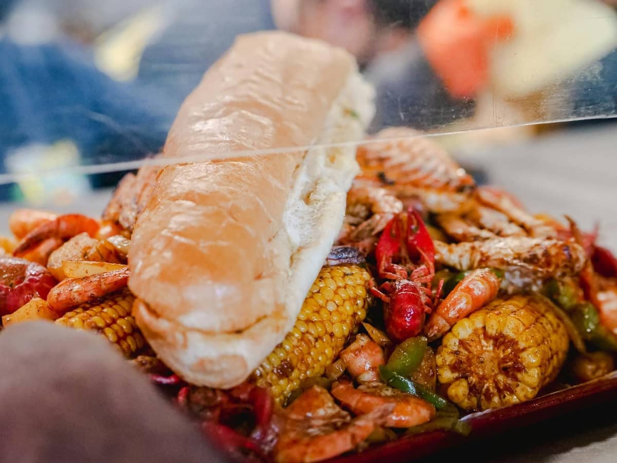 Close-up of a New Orleans seafood boil platter with crawfish, shrimp, corn, and a po' boy sandwich on top.