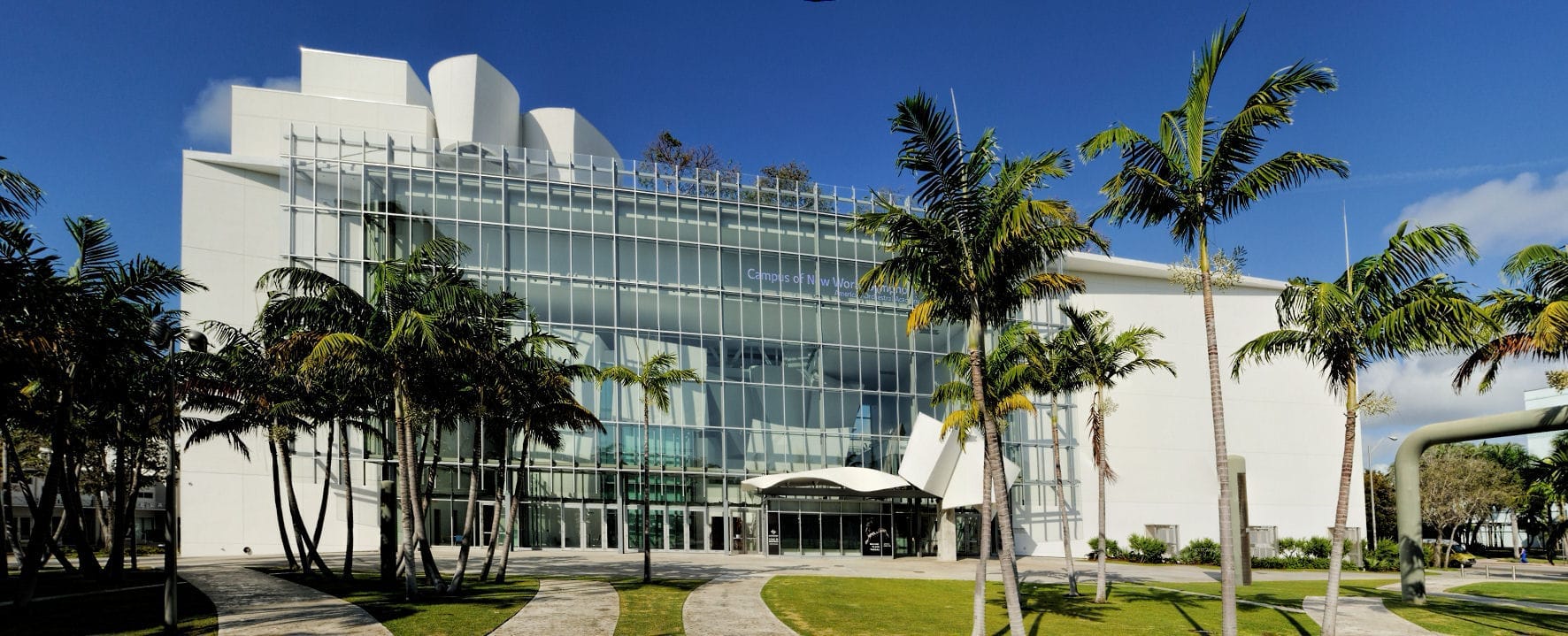 Moderna facciata in vetro della sala concerti New World Center, circondata da palme e cieli azzurri a Miami Beach, Florida.