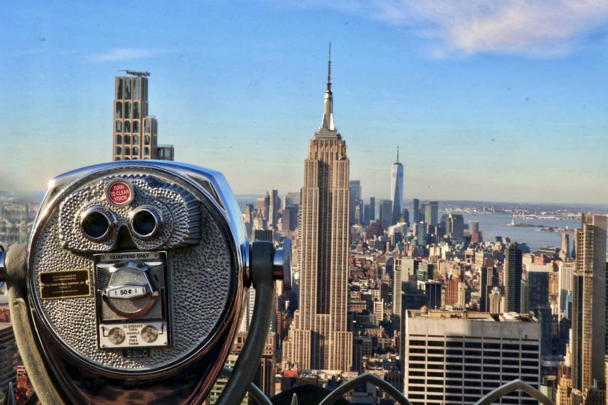 กล้องส่องทางไกลแบบคลาสสิกบนจุดชมวิว พร้อมวิวของ Empire State Building และเส้นขอบฟ้าของ New York City ในวันที่อากาศแจ่มใส