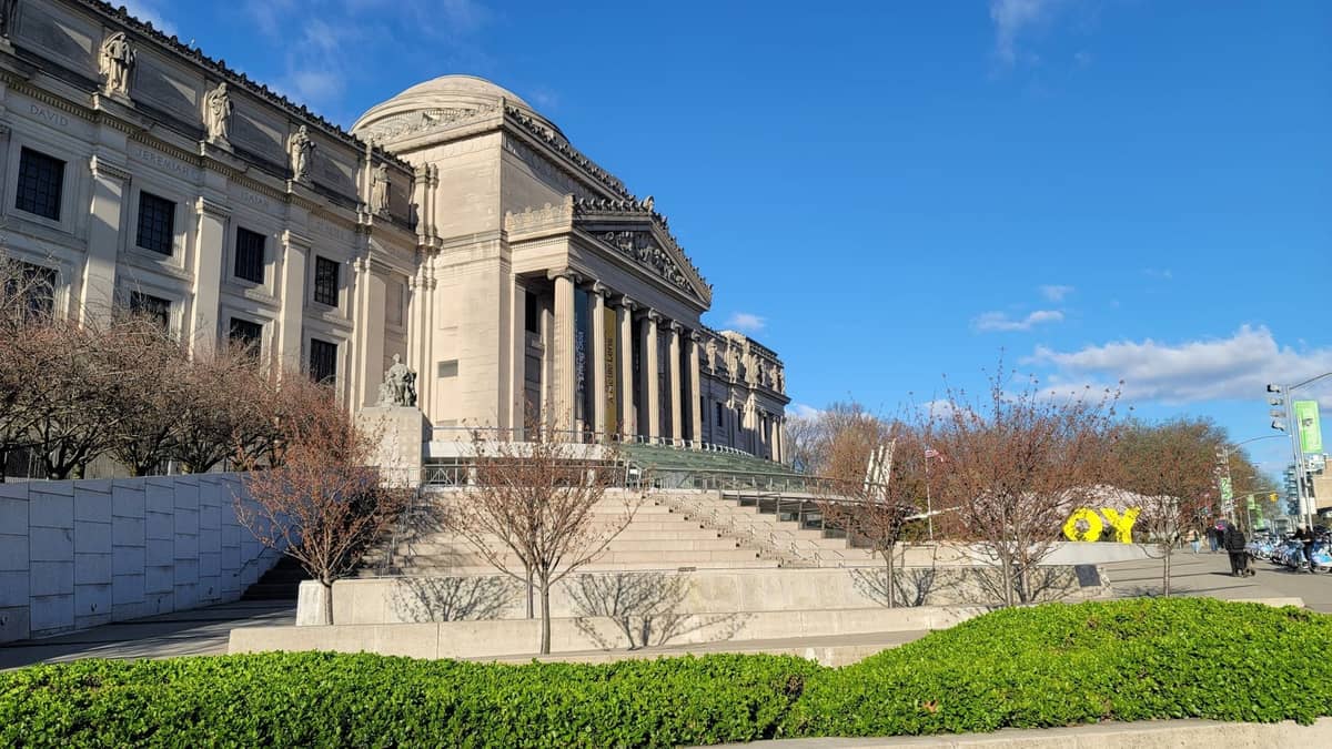 อาคารพิพิธภัณฑ์สไตล์ Grand Beaux-Arts พร้อมเสาและรายละเอียดงานประติมากรรม ถ่ายภาพจากลานกว้างในแสงกลางวันที่สดใส