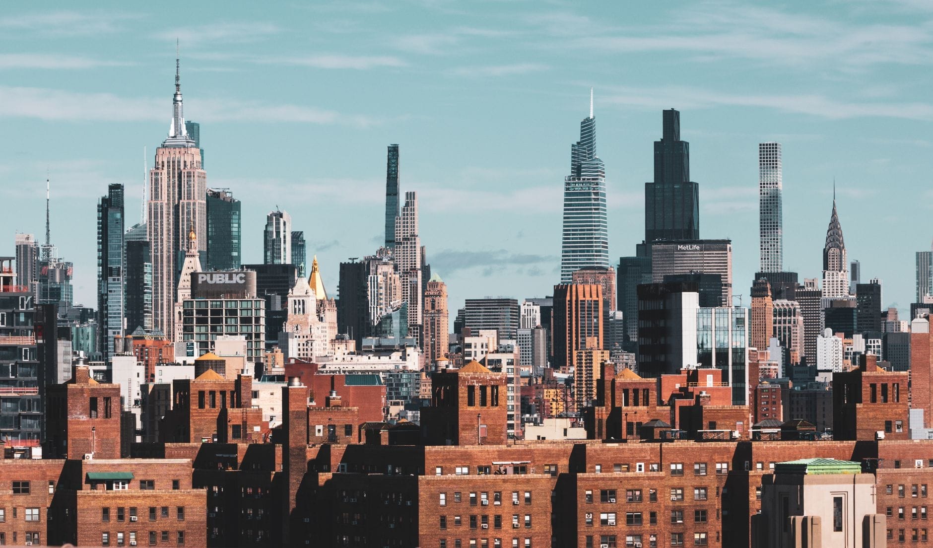 Panorâmica ampla do skyline de Nova York com destaque para arranha-céus icônicos, incluindo o Empire State Building, torres modernas e edifícios históricos sob um céu aberto.