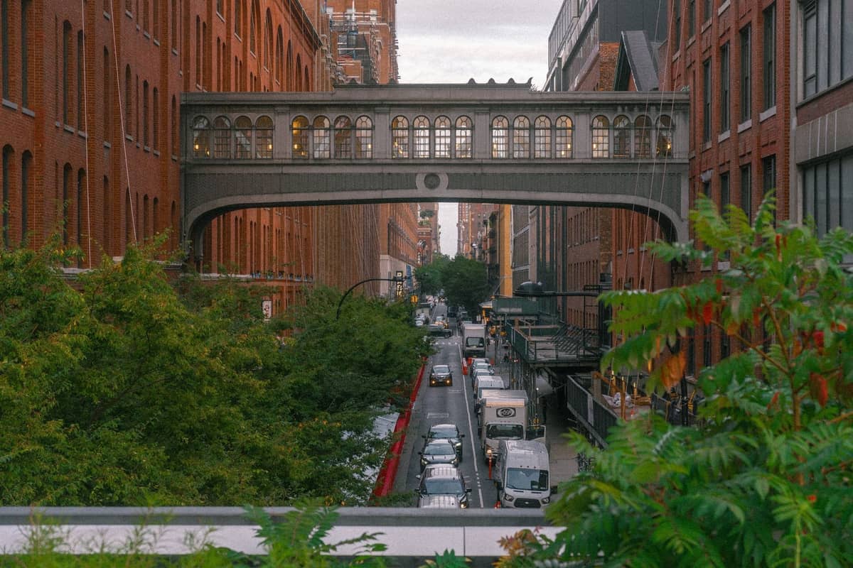 Ein Blick auf das Galerieviertel Chelsea in New York City, mit der erhöhten Hängebrücke über einer Straße gesäumt von Backsteingebäuden, Bäumen und lebhaftem Verkehr darunter.