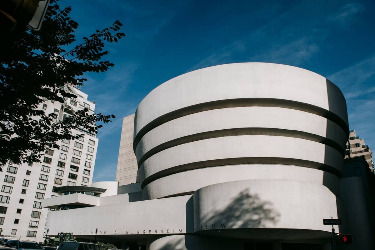 Außenansicht der ikonischen gerundeten weißen Fassade des Guggenheim Museum vor einem blauen Himmel in New York City mit umliegenden Gebäuden.