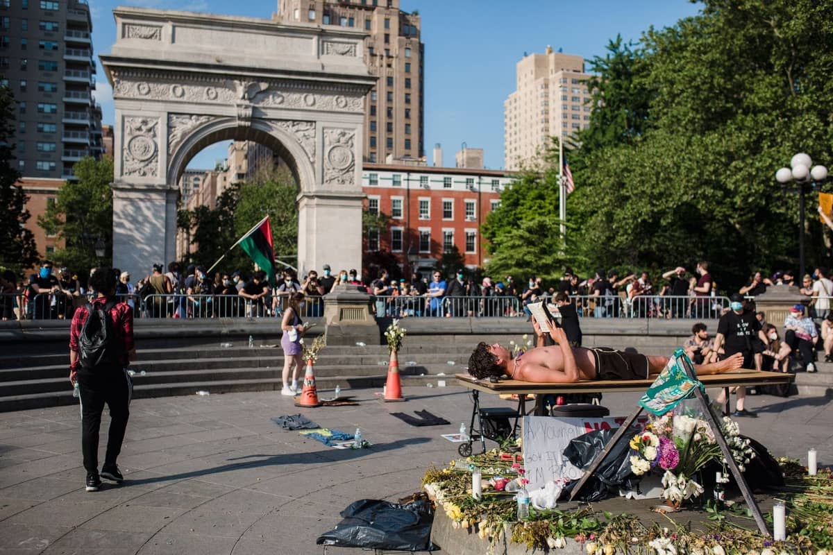 Menschen versammeln sich und entspannen im Washington Square Park mit dem ikonischen Bogen im Hintergrund an einem sonnigen Tag in New York City.