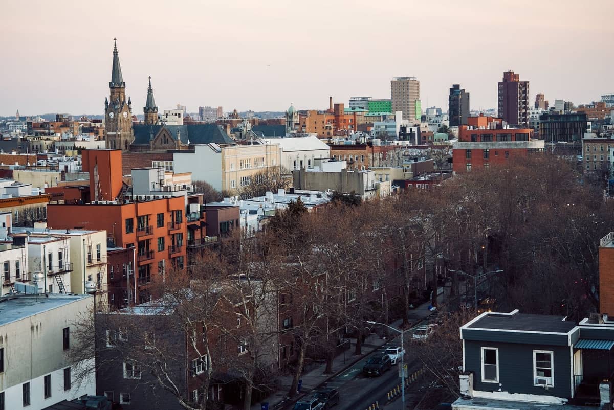 Luftaufnahme eines Stadtteils von New York City mit einer Mischung aus niedrigen Gebäuden, Kirchen und baumgesäumten Straßen in der Dämmerung.