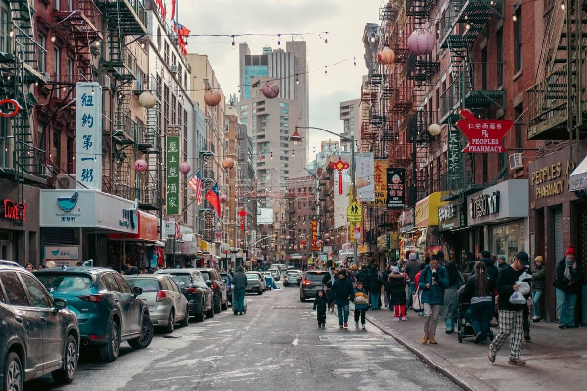Belebte Straßenszene in Chinatown in New York City mit verschiedenen Geschäften, Passanten und hängenden Laternen, die die multikulturelle Esskultur der Stadt widerspiegeln.