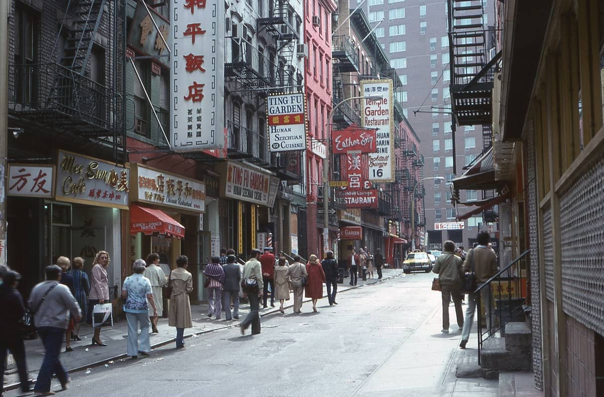 Belebte Straße in New York Citys Chinatown mit Fußgängern, chinesischen Restaurantschildern und städtischen Gebäuden.