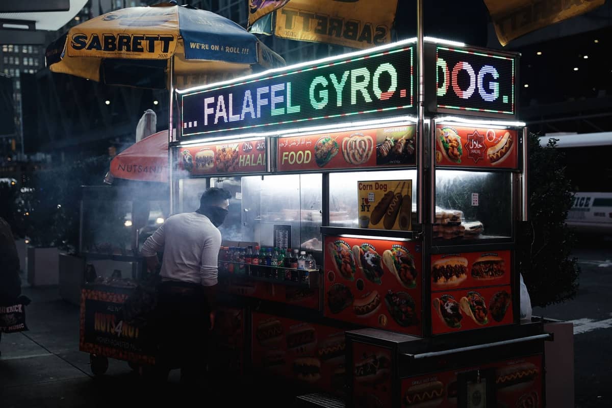 Nächtliche Szene eines klassischen Straßenimbisswagens in New York City, der Halal-Essen verkauft, hell beleuchtet, mit einer Person, die eine Bestellung aufgibt.