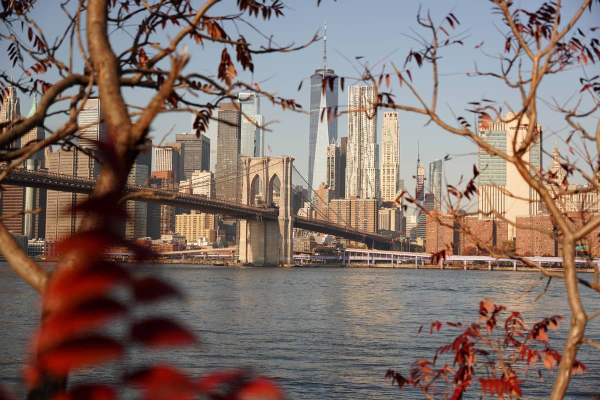 Brooklyn Bridge und die Skyline von Manhattan, eingerahmt von bunten Herbstästen, mit klarem Licht und frischer saisonaler Atmosphäre.