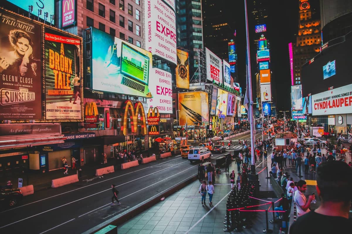 Nächtlicher Blick auf den Times Square in New York City mit hell leuchtenden Theaterwerbetafeln, Neonlichtern und Menschenmassen, die die Aufregung der Broadway-Shows heraufbeschwören.