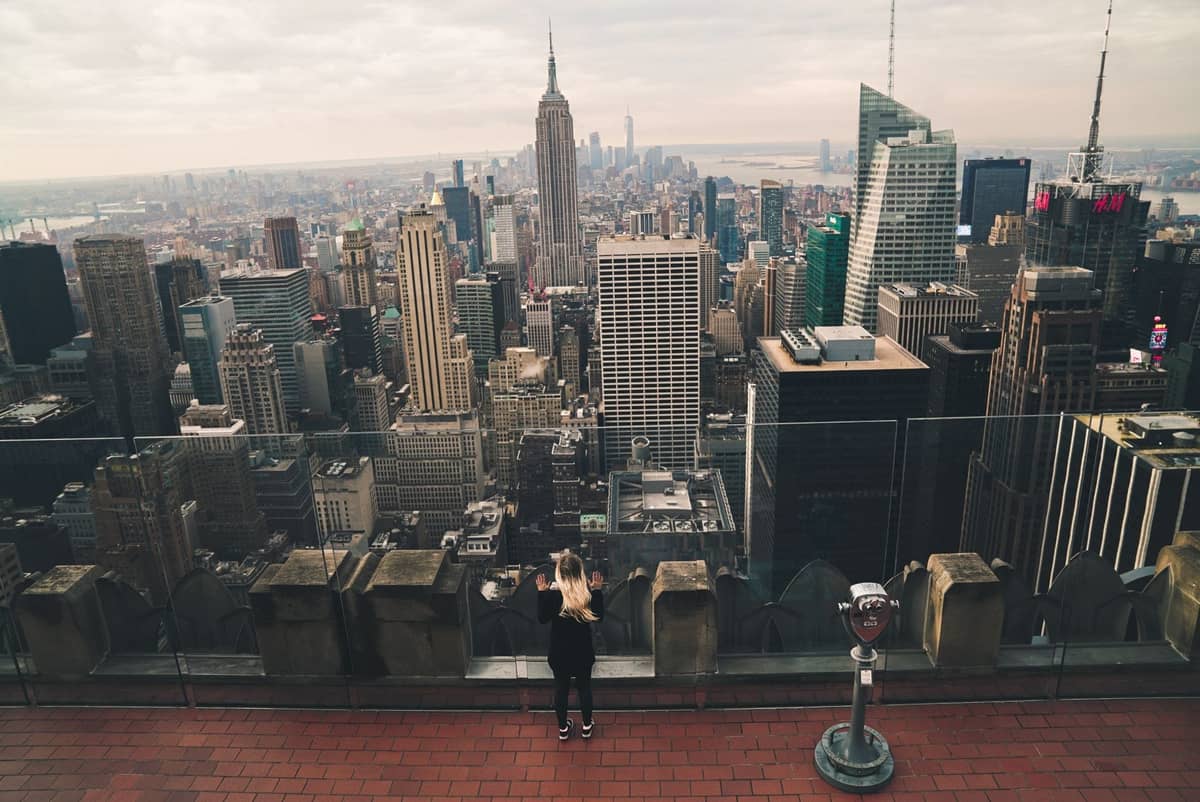 Person, die von der Aussichtsplattform Top of the Rock auf die Skyline von New York City mit dem Empire State Building blickt.