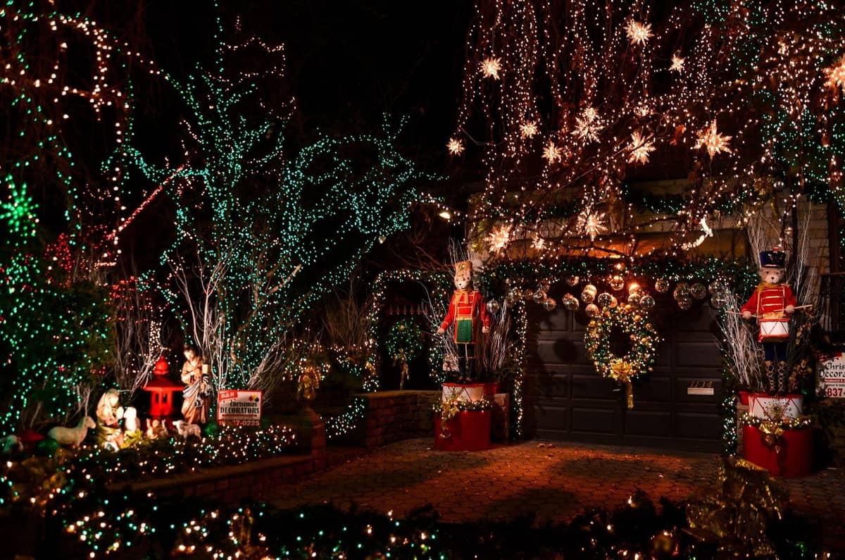 Ein hell dekoriertes Haus bei Nacht mit aufwendigen Feiertagslichtern, beleuchteten Bäumen, Kränzen und großen Nussknacker-Dekorationen in einer Wohngegend.