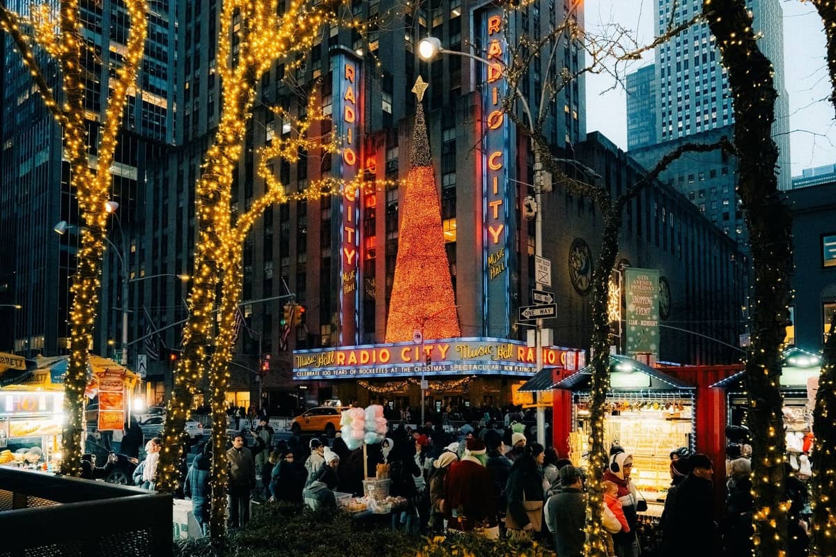 Radio City Music Hall bei Nacht während der Feiertage, mit einem großen beleuchteten Weihnachtsbaum und festlichen Lichtern, Menschenmassen draußen.