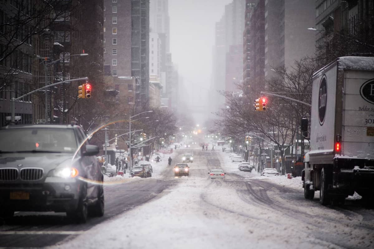 Verschneite Straße in New York City mit Autos, Gebäuden und Ampeln an einem kalten Wintertag im Dezember.