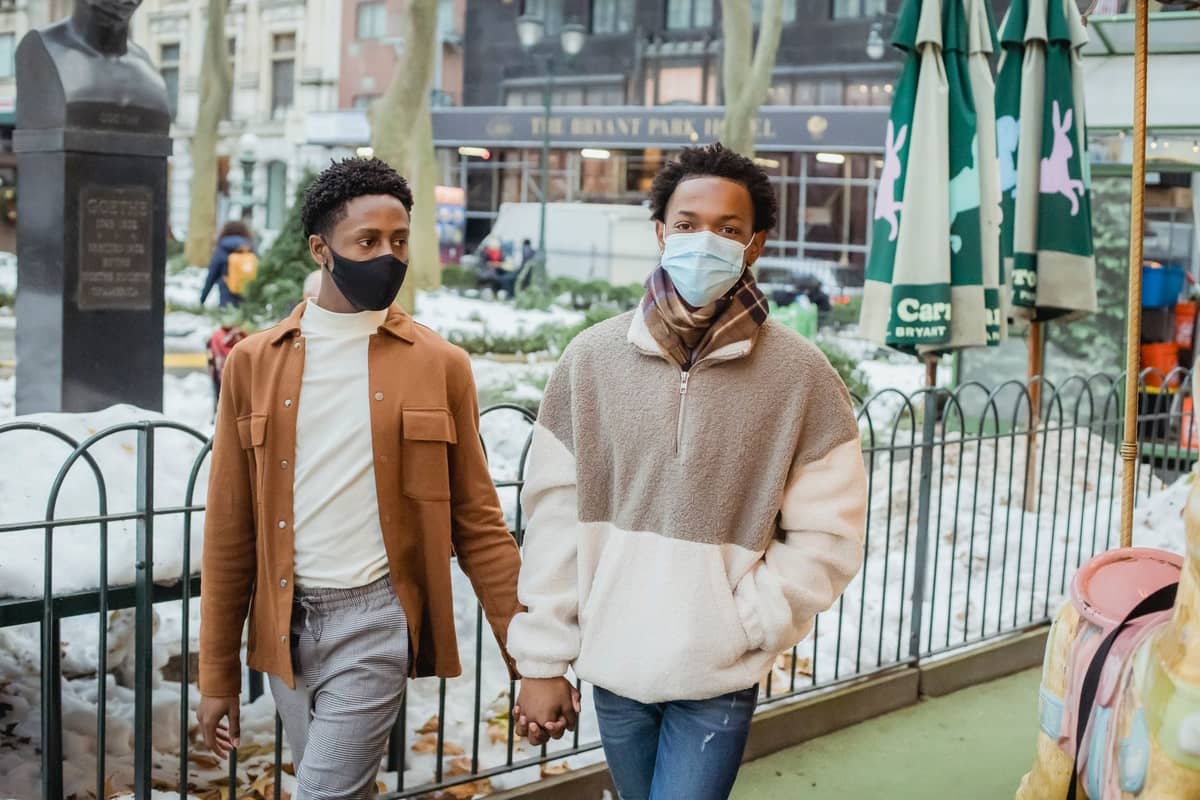 Zwei Personen mit Masken spazieren draußen im Bryant Park, im Hintergrund sind Wintermarktstände und Schnee zu sehen.