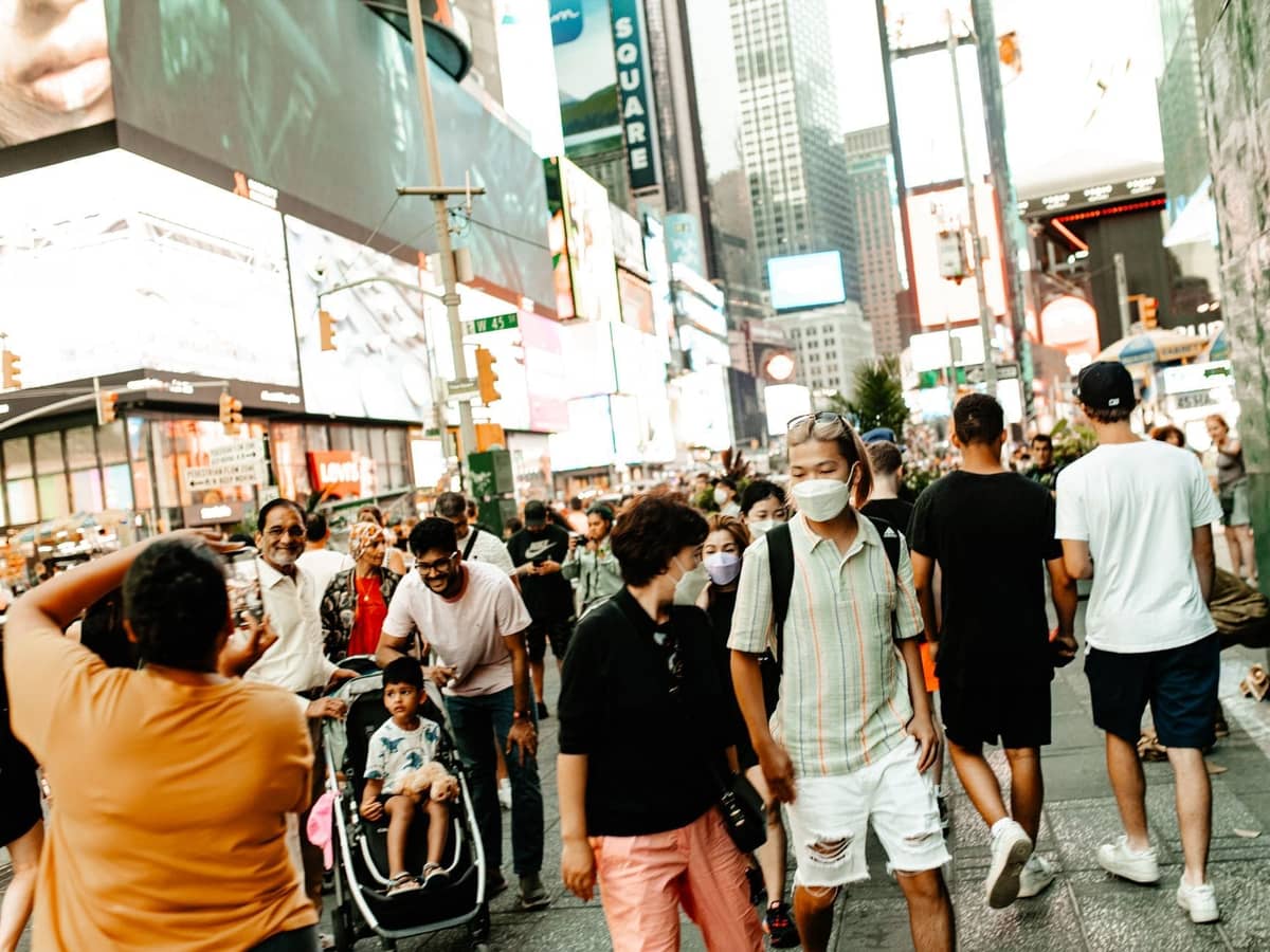 Große Menschenmenge, die an einem Sommertag durch den sonnenbeschienenen Times Square in New York City läuft.