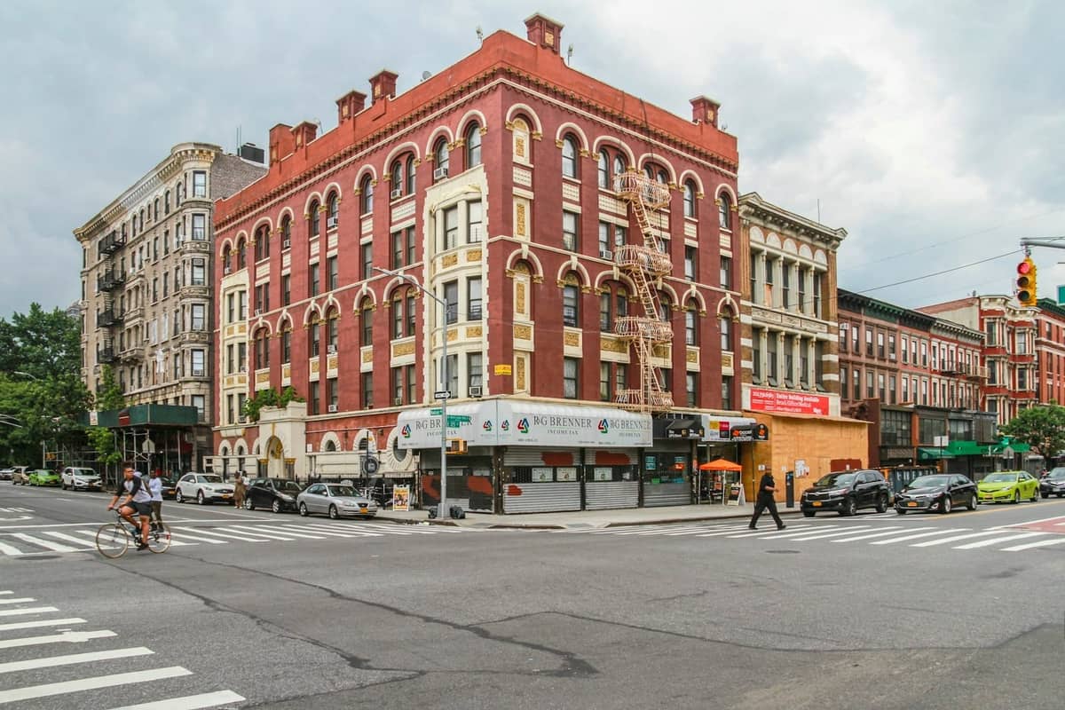 Historisches Backsteingebäude an einer Straßenecke in Harlem in New York City, mit Bogenfenstern und Straßenleben, das die lokale Jazz-Architektur veranschaulicht.