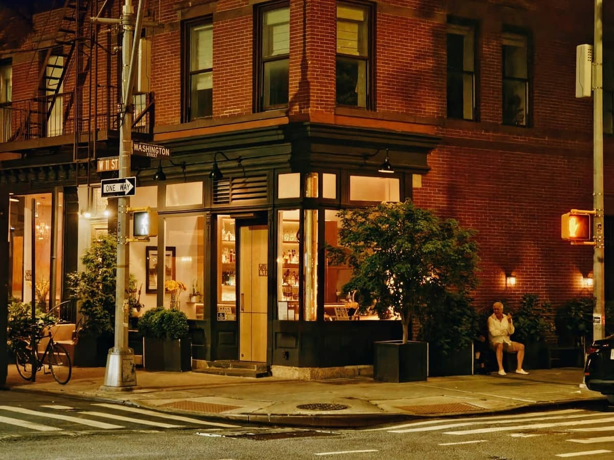 Warm beleuchtetes Eckgebäude in Greenwich Village bei Nacht mit einer draußen sitzenden Person, klassische Backsteinarchitektur aus NYC.