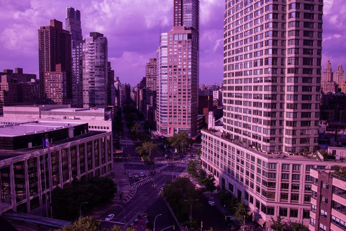 Weitläufige Aussicht auf das Lincoln Center und die umliegenden Hochhäuser in New York City, aufgenommen in der Abenddämmerung mit einem violetten Farbton über der Stadtlandschaft.