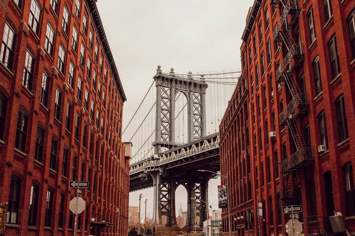 Blick auf die Manhattan Bridge, eingerahmt von roten Backsteingebäuden in DUMBO, Brooklyn unter einem bewölkten Himmel.
