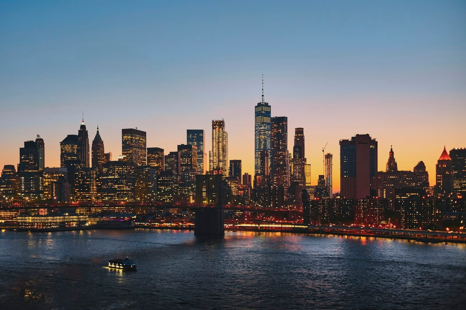 Vista panorâmica do skyline de Nova York ao pôr do sol, com arranha-céus de vários bairros e o Rio East em primeiro plano.