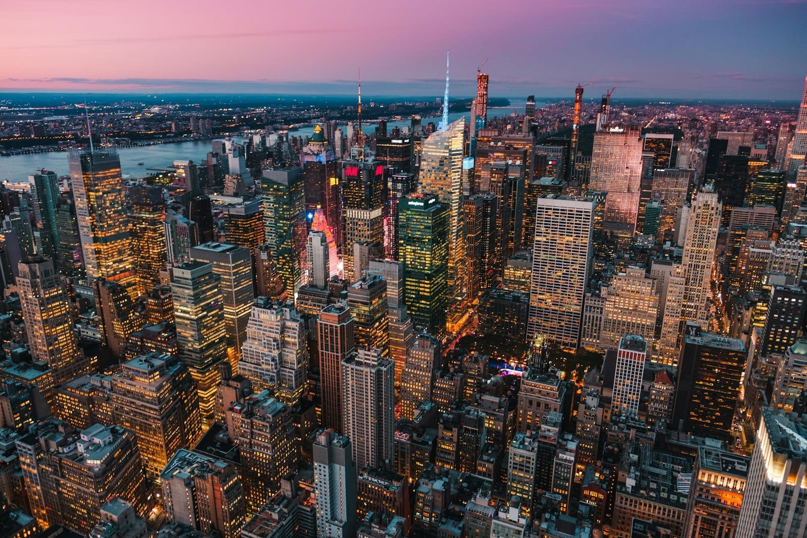 Vista aérea de Midtown Manhattan ao entardecer, com a Times Square e os arranha-céus iluminados capturando a vibrante skyline de Nova York em clima de festa.