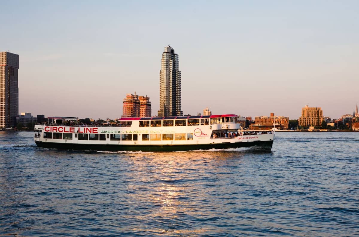 Circle Line Party-Kreuzfahrtschiff auf dem Wasser mit der Skyline von New York City im Hintergrund bei Sonnenuntergang.