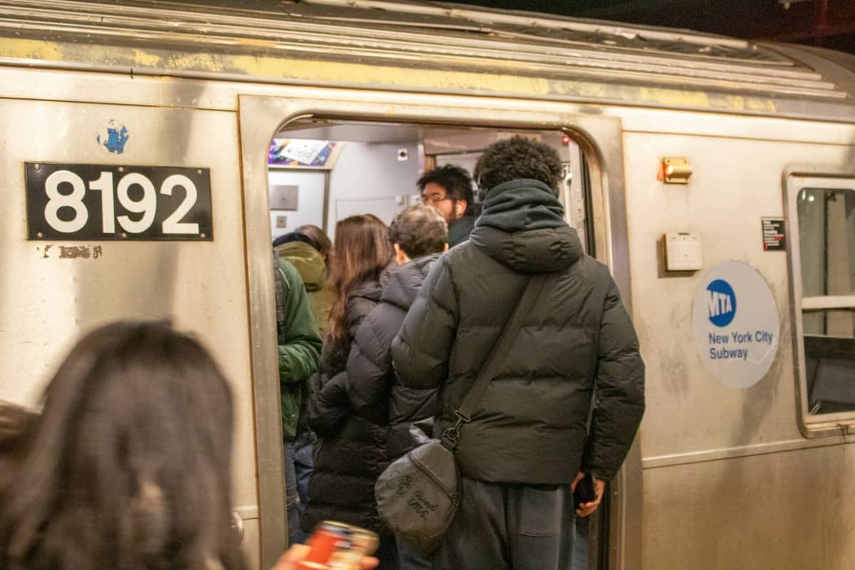 Menschenmenge beim Einsteigen in eine New York City U-Bahn bei Nacht, mit sichtbarem MTA-Logo und Zugnummer.