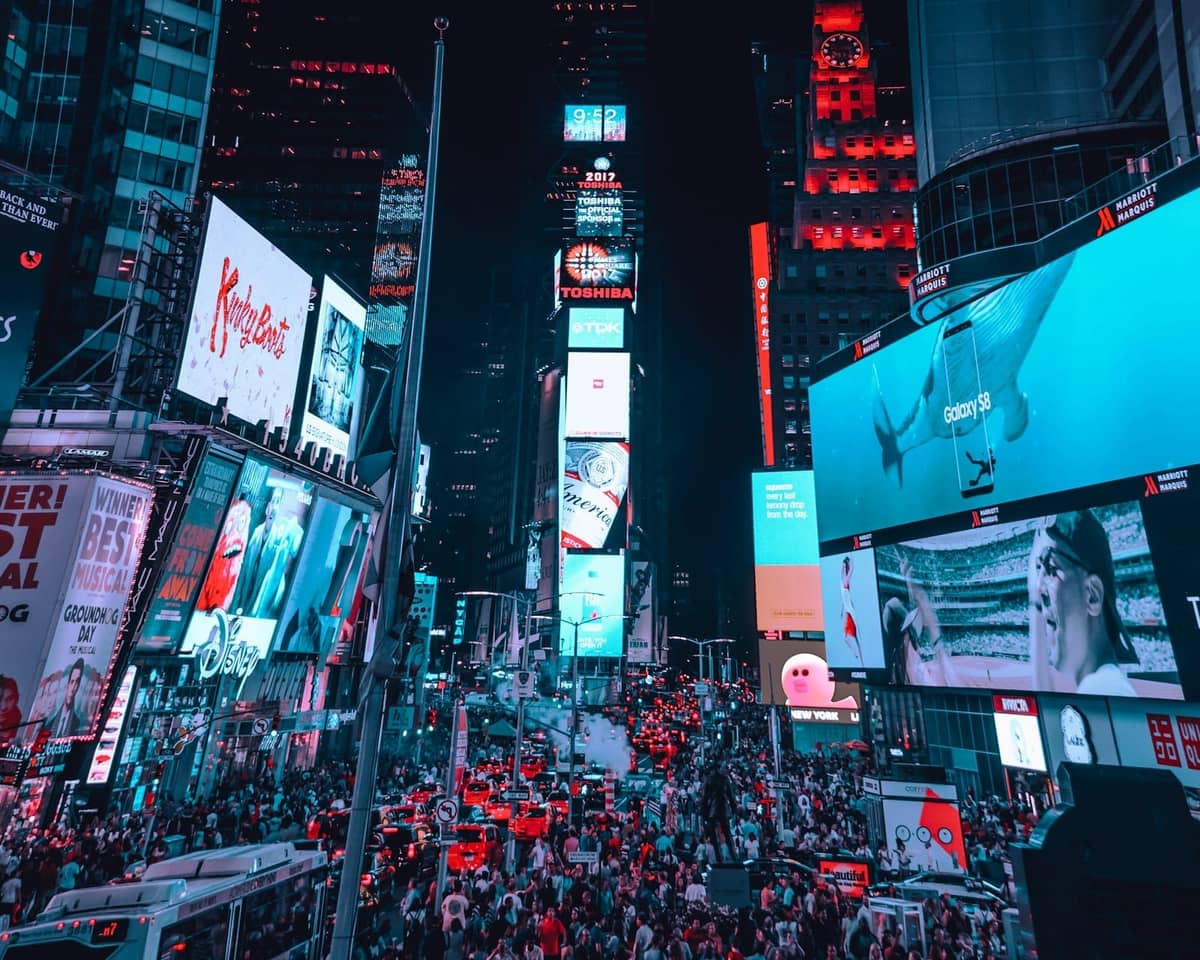 Überfüllter Times Square bei Nacht mit hellen Werbetafeln und dem One Times Square-Gebäude, wo der Silvester-Ballabwurf stattfindet.