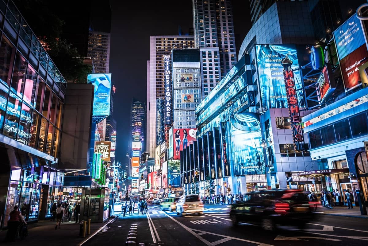 วิวของ Times Square ยามค่ำคืนพร้อมป้ายนีออนสว่างไสว ถนนที่คึกคัก และผู้คนที่เดินอยู่ท่ามกลางอาคารอันเป็นสัญลักษณ์ของ New York City