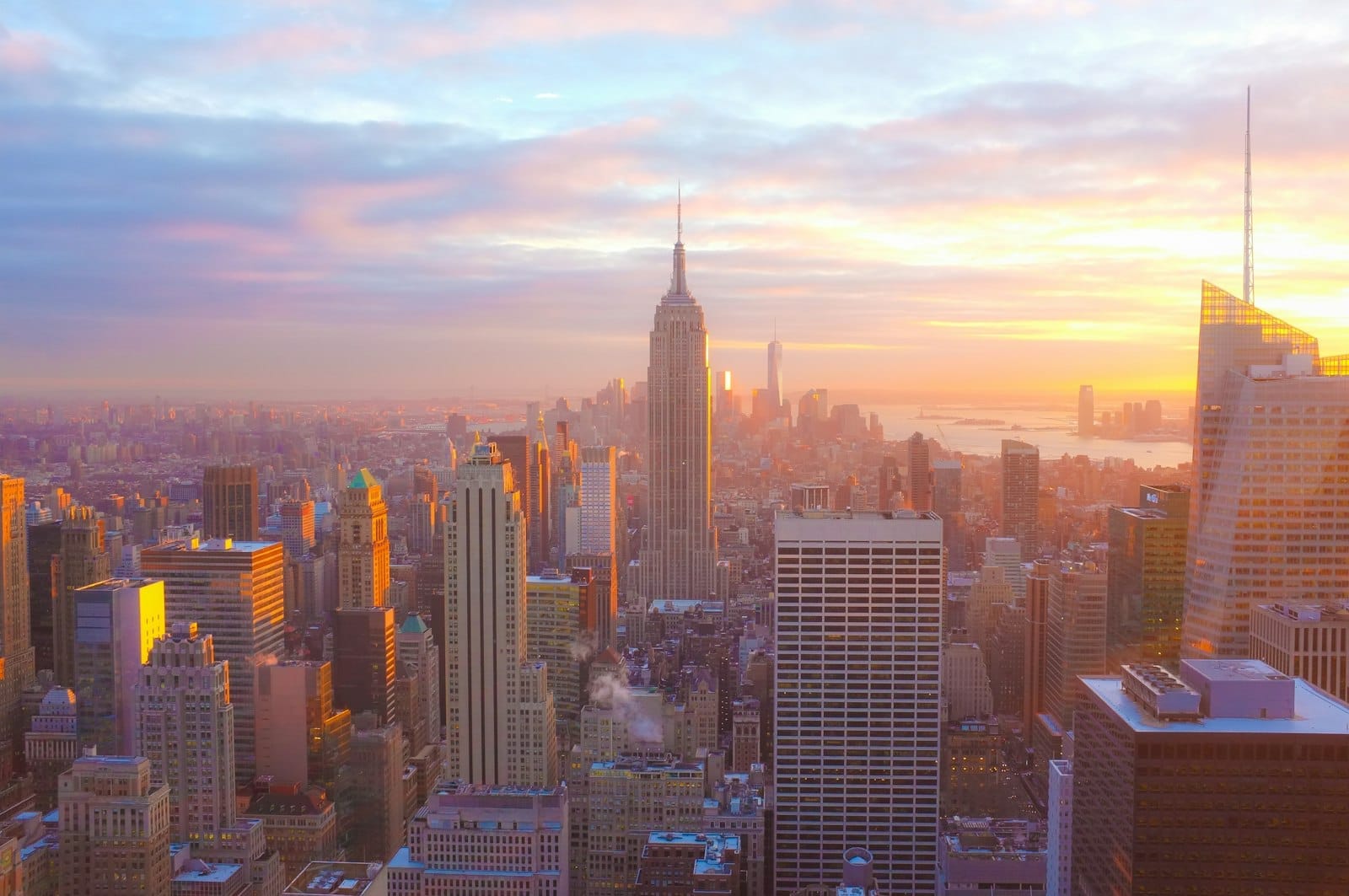 Um amanhecer vibrante sobre o skyline de Nova York com o Empire State Building e os arranha-céus ao redor banhados por uma luz quente e convidativa. Perfeito para viajantes.