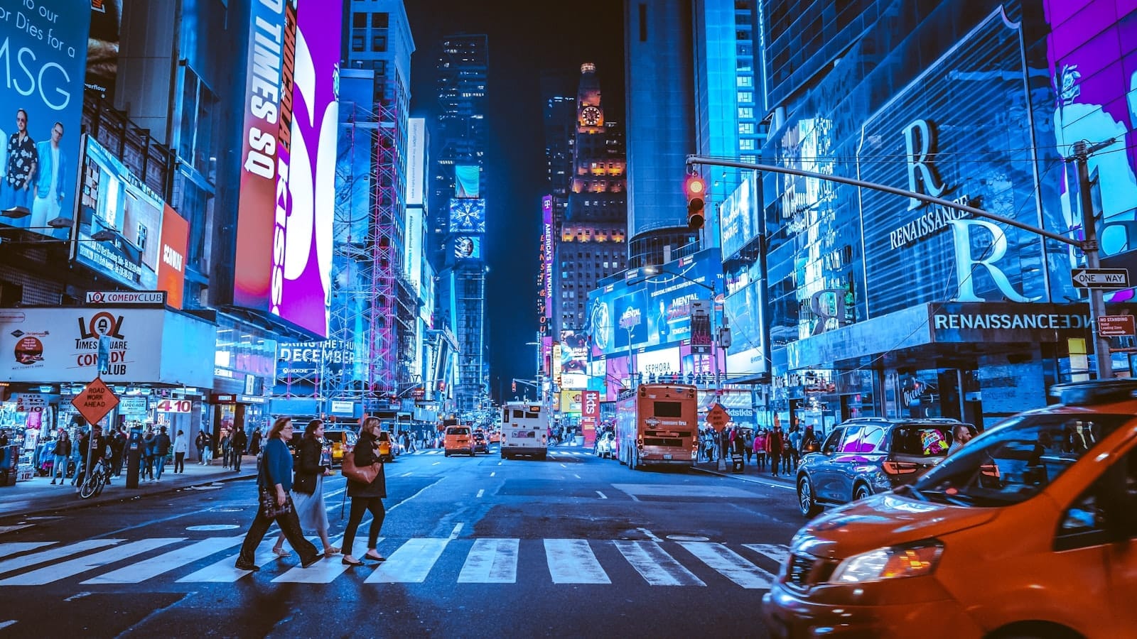 Vista noturna da Times Square em Nova York com pedestres atravessando a rua, táxis, letreiros de néon brilhantes e muita energia.