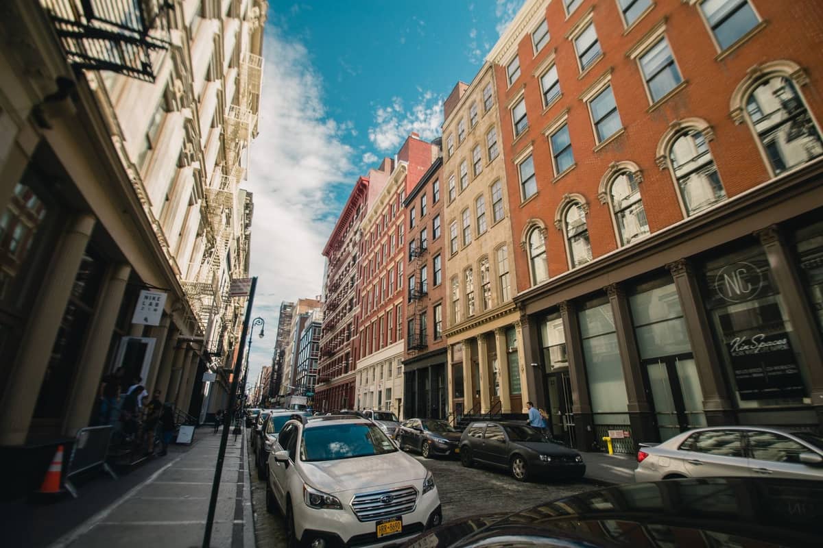 ภาพถนนคลาสสิกในย่าน SoHo กรุงนิวยอร์กซิตี้ พร้อมอาคารเหล็กหล่อ รถยนต์จอดเรียงรายตามถนนที่ปูด้วยหินกรวด และท้องฟ้าสีฟ้า