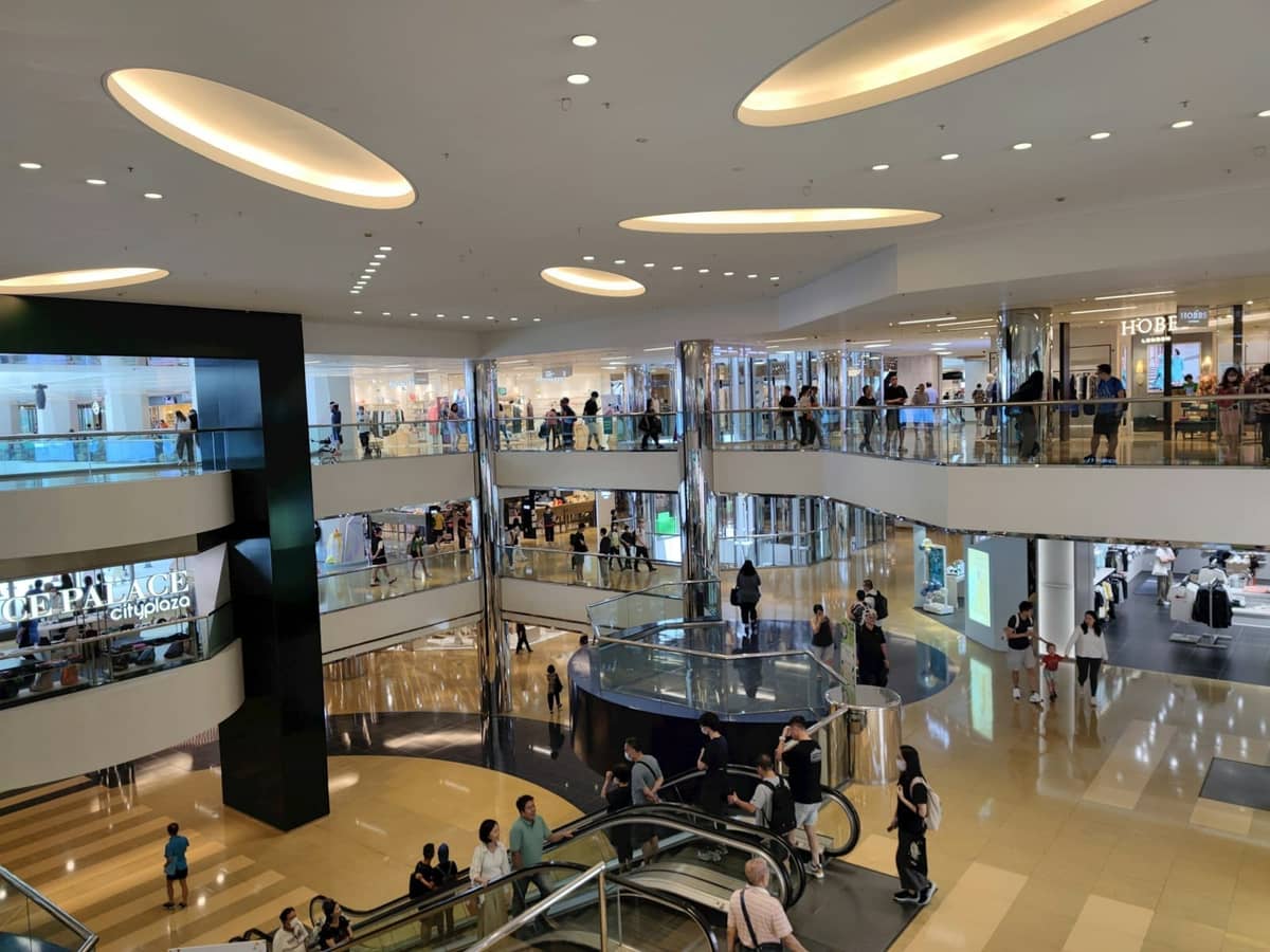 ภายในห้างสรรพสินค้าสมัยใหม่หลายชั้นที่คึกคัก มีนักช้อป บันไดเลื่อน และร้านค้าระดับไฮเอนด์ให้เห็น
