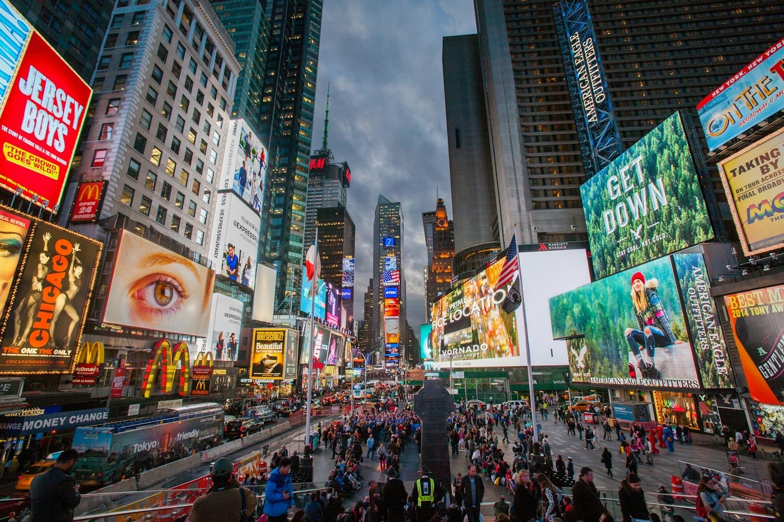 Vista ampla da Times Square em Nova York lotada de pessoas, outdoors coloridos, ruas movimentadas e luzes vibrantes da cidade ao entardecer.