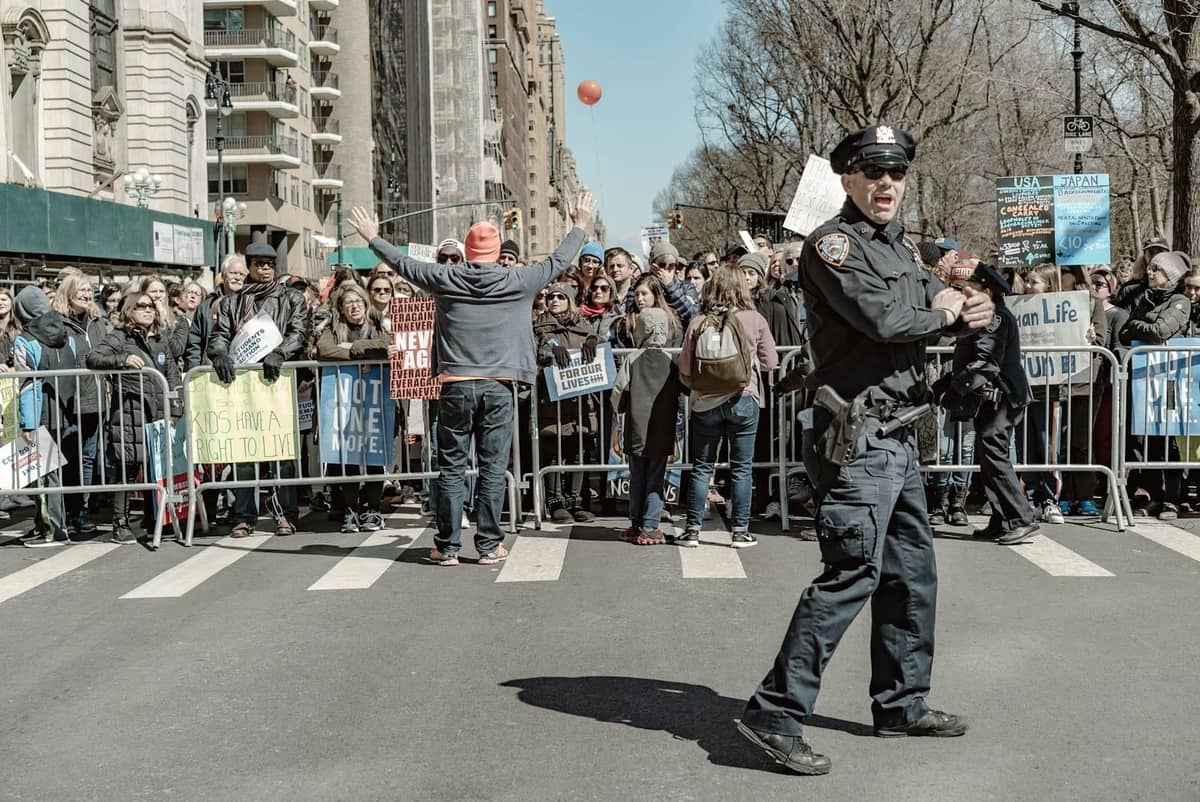 ฝูงชนอยู่เบื้องหลังแนวกั้นบนถนนใน New York City พร้อมเจ้าหน้าที่ตำรวจดูแลเส้นทางขบวนพาเหรด