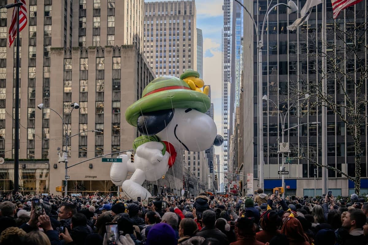 บอลลูน Snoopy ขนาดใหญ่ลอยอยู่เหนือฝูงชนในงาน Macy's Thanksgiving Day Parade ที่นิวยอร์กซิตี้ ล้อมรอบด้วยตึกสูงของแมนฮัตตัน