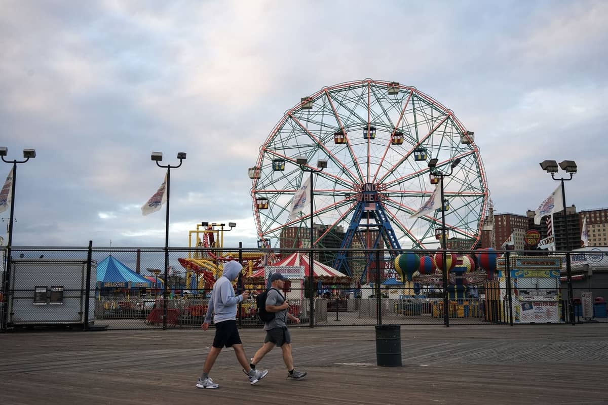 วิวกว้างของทางเดินริมชายหาด Coney Island พร้อมผู้คนที่เดินอยู่ด้านหน้า Wonder Wheel อันโด่งดังและเครื่องเล่นในสวนสนุก