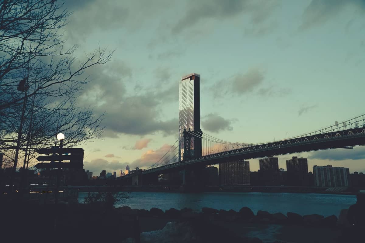 Blick auf die Brooklyn Bridge bei Sonnenuntergang mit einem teilweise bewölkten Himmel und der Skyline von New York City im Hintergrund.