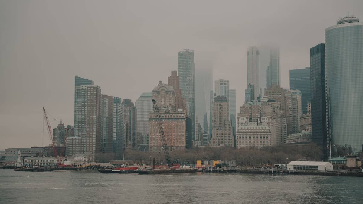Bewölkter Blick auf die Skyline von Lower Manhattan von der anderen Flussseite, mit hohen Wolkenkratzern, die teilweise von Nebel und Wolken verdeckt werden.