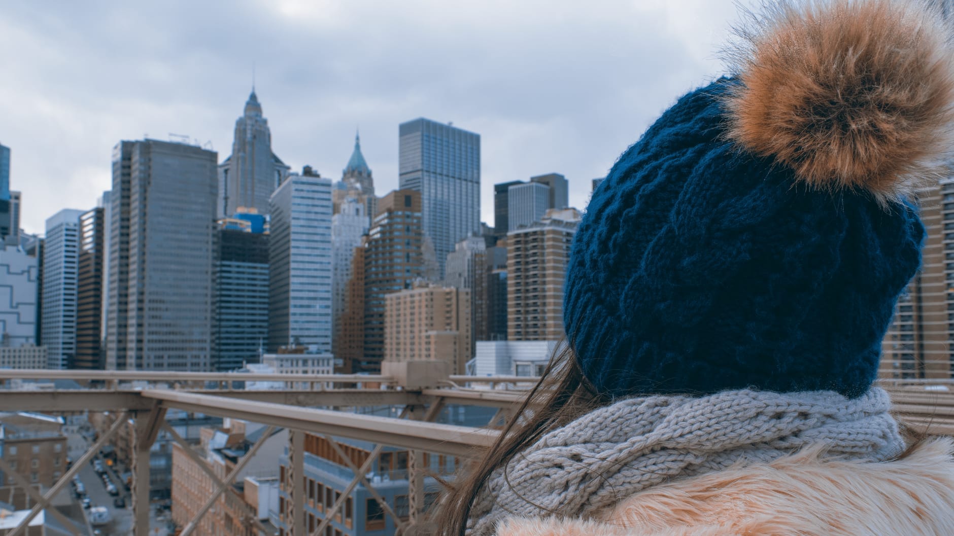 Uma pessoa com touca e cachecol observa o skyline de Nova York em um dia frio e nublado, evidenciando as mudanças climáticas da cidade.